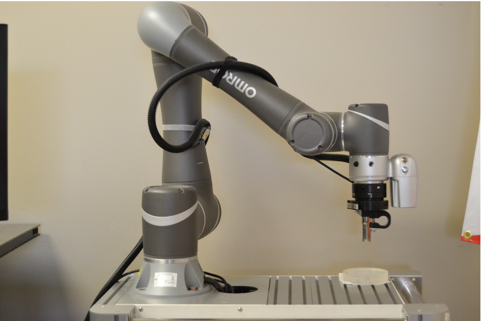 A picture of a collaborative robot with an OptiGauge Probe attached to the end of the arm. It is measuring a material sample.